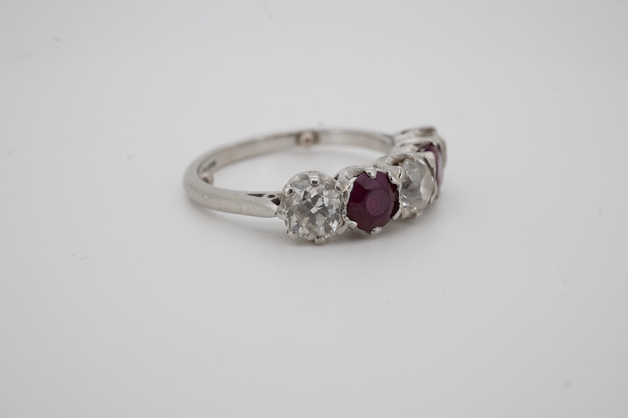 A ruby and diamond five-stone ring, set with an alternating sequence of antique cushion-shaped diamonds totalling approximately 1.50 carats, spaced with circular-cut rubies, mounted in platinum, size M (sizing beads), Br